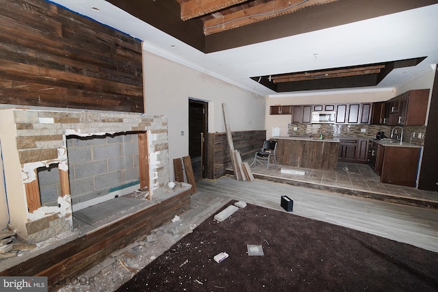 unfurnished living room featuring a tray ceiling, sink, crown molding, and a stone fireplace