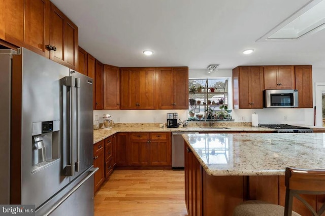 kitchen featuring a breakfast bar area, stainless steel appliances, light stone counters, light hardwood / wood-style flooring, and sink