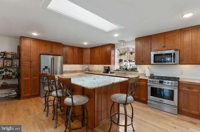 kitchen featuring a breakfast bar area, appliances with stainless steel finishes, light hardwood / wood-style floors, a skylight, and a center island