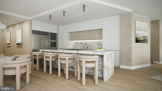 kitchen with a kitchen breakfast bar, light hardwood / wood-style floors, built in refrigerator, white cabinets, and a center island