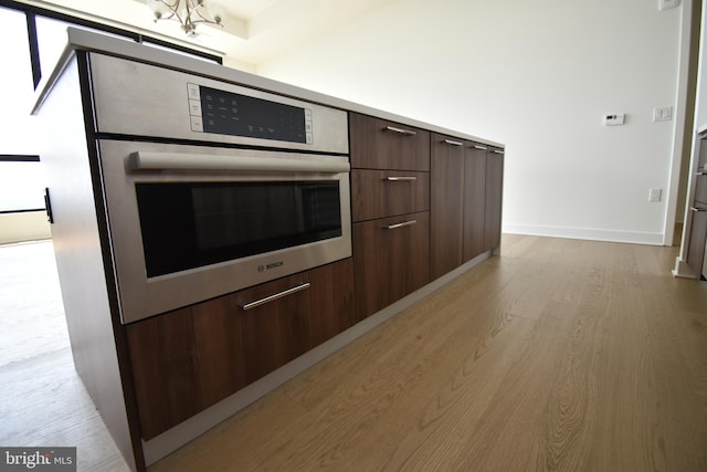 kitchen featuring stainless steel oven, light hardwood / wood-style floors, and dark brown cabinets