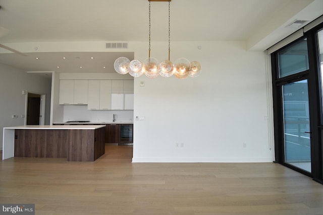 kitchen featuring white cabinetry, light hardwood / wood-style flooring, a kitchen island, pendant lighting, and beverage cooler