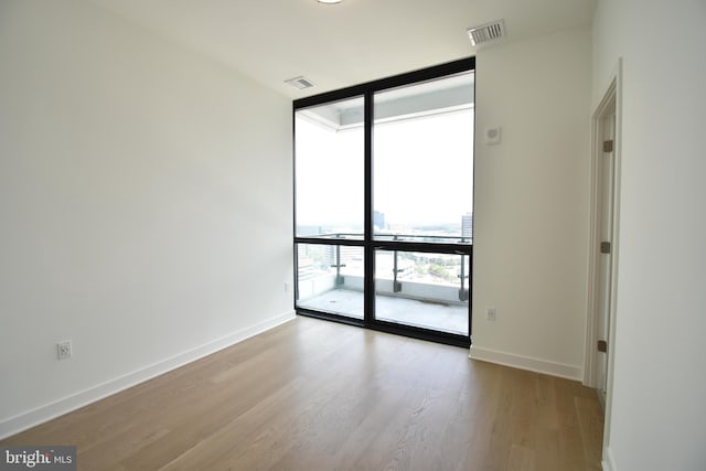 empty room featuring a wall of windows and light hardwood / wood-style floors