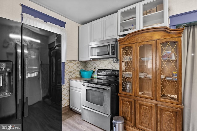 kitchen with stainless steel appliances, white cabinets, and light wood-type flooring