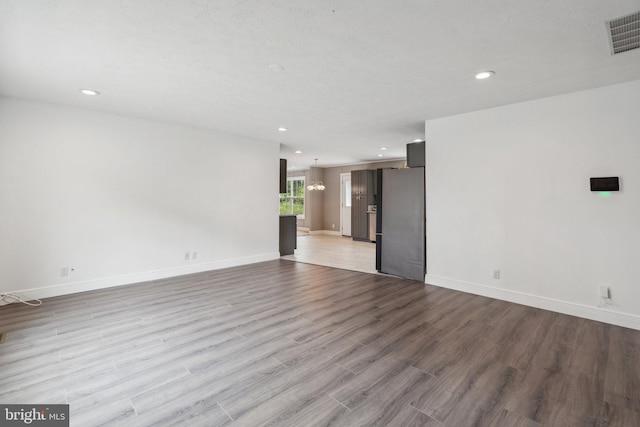 unfurnished living room with recessed lighting, wood finished floors, visible vents, baseboards, and an inviting chandelier