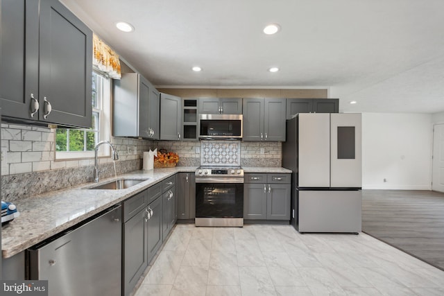 kitchen with light stone counters, a sink, stainless steel appliances, backsplash, and recessed lighting