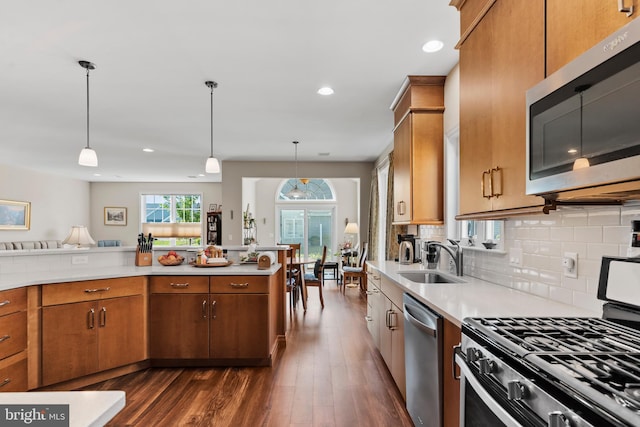 kitchen with sink, dark wood-type flooring, stainless steel appliances, decorative backsplash, and decorative light fixtures