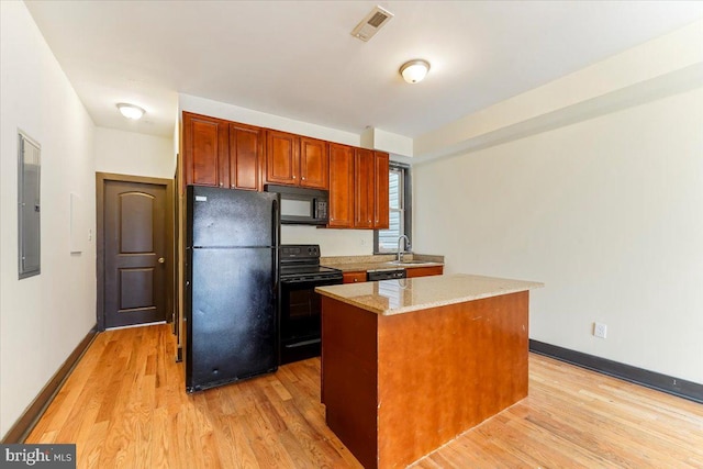 kitchen with black appliances, light stone countertops, light hardwood / wood-style floors, a kitchen island, and sink