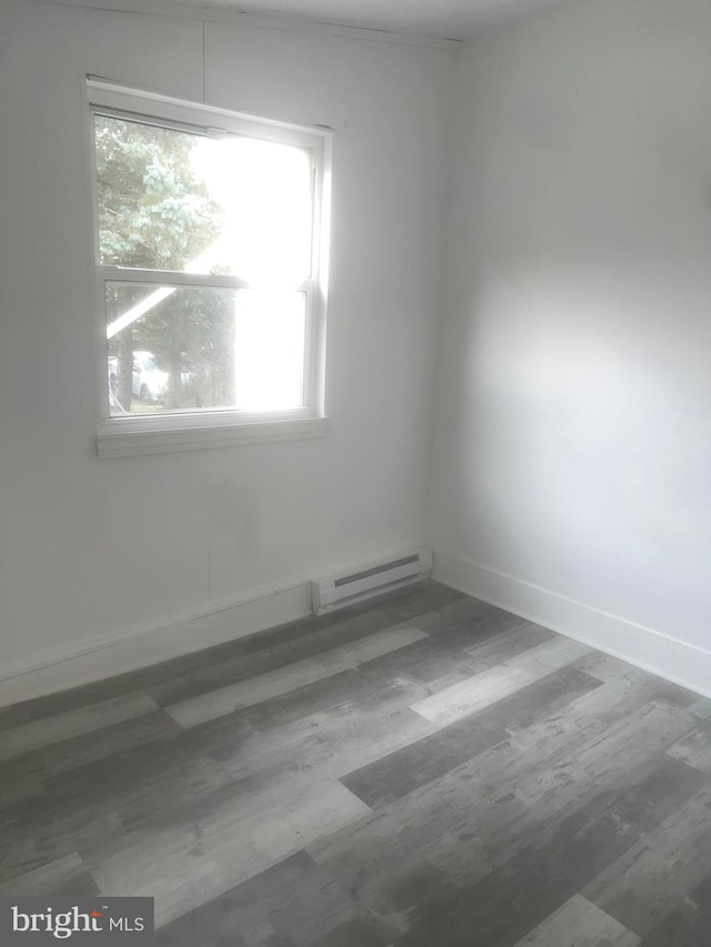 empty room featuring baseboard heating, a healthy amount of sunlight, and hardwood / wood-style flooring