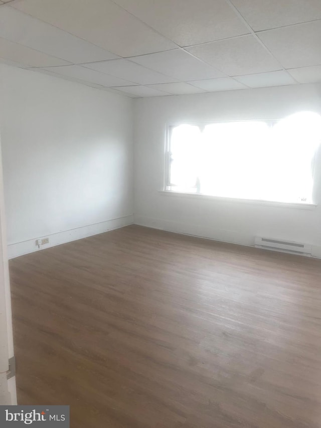 unfurnished room with a drop ceiling, baseboard heating, and hardwood / wood-style flooring