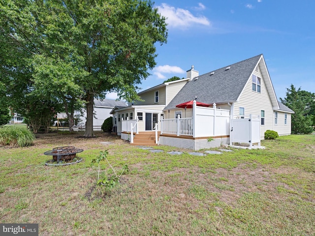 back of house featuring a wooden deck, a lawn, and an outdoor fire pit