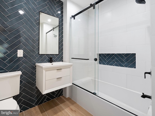 full bathroom with toilet, tile walls, wood-type flooring, shower / bath combination with glass door, and vanity