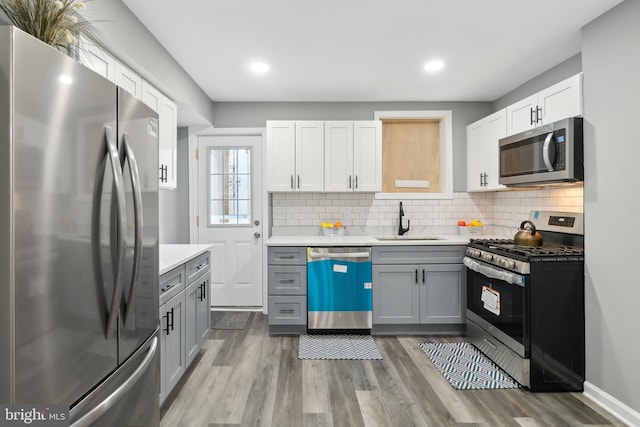 kitchen with wood finished floors, gray cabinetry, a sink, light countertops, and appliances with stainless steel finishes