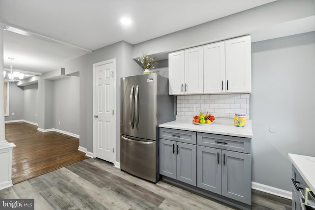 kitchen featuring gray cabinetry, wood finished floors, freestanding refrigerator, decorative backsplash, and baseboards