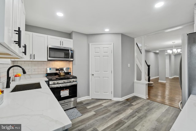 kitchen with decorative light fixtures, appliances with stainless steel finishes, light stone countertops, light hardwood / wood-style floors, and sink