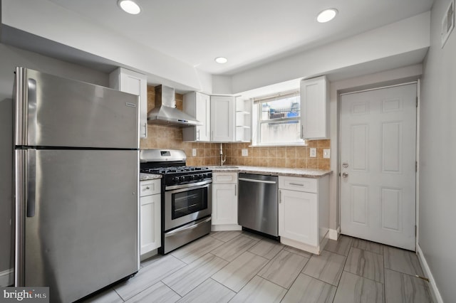 kitchen with stainless steel appliances, white cabinetry, tasteful backsplash, sink, and wall chimney range hood