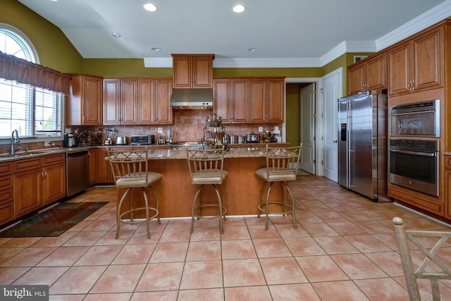 kitchen with stainless steel appliances, a kitchen breakfast bar, light stone counters, a kitchen island, and lofted ceiling