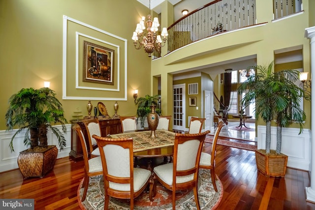 dining area featuring a wainscoted wall, visible vents, wood finished floors, an inviting chandelier, and a towering ceiling