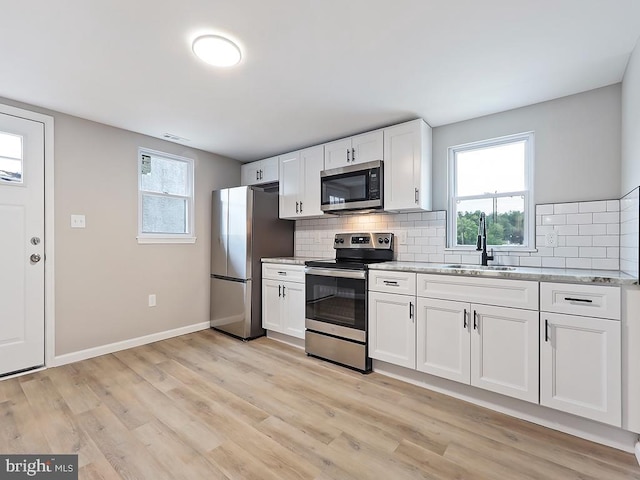 kitchen with stainless steel appliances, light wood-type flooring, sink, tasteful backsplash, and white cabinetry