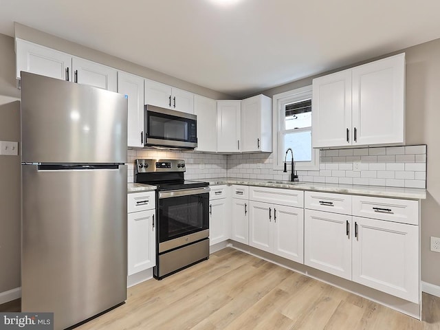 kitchen featuring light hardwood / wood-style flooring, white cabinetry, appliances with stainless steel finishes, backsplash, and sink