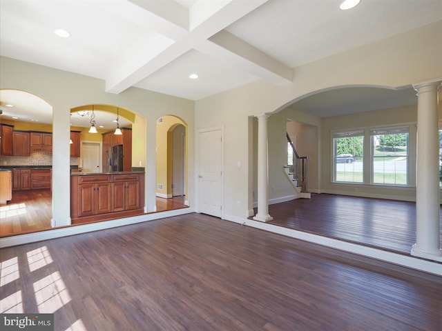 unfurnished living room featuring dark wood-type flooring, beam ceiling, and ornate columns