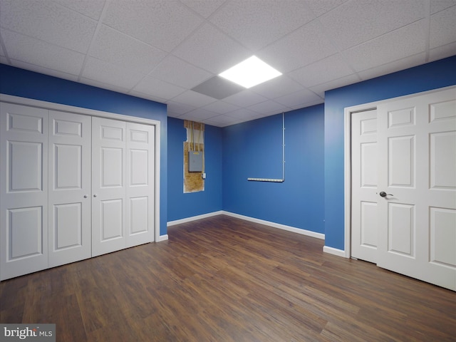 unfurnished bedroom featuring electric panel, dark wood-type flooring, a paneled ceiling, and a closet