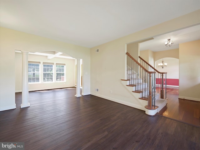 unfurnished living room with dark wood-type flooring, a chandelier, and ornate columns