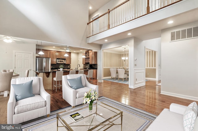 living room with light hardwood / wood-style flooring, ceiling fan with notable chandelier, and a towering ceiling