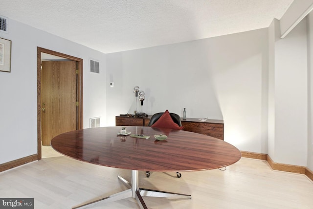 dining room with light wood-type flooring and a textured ceiling