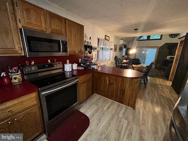 kitchen featuring kitchen peninsula, light hardwood / wood-style flooring, a textured ceiling, and stainless steel appliances