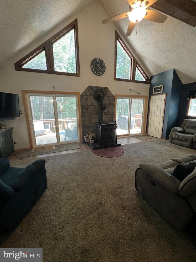 living room with high vaulted ceiling, a textured ceiling, carpet flooring, and a wood stove