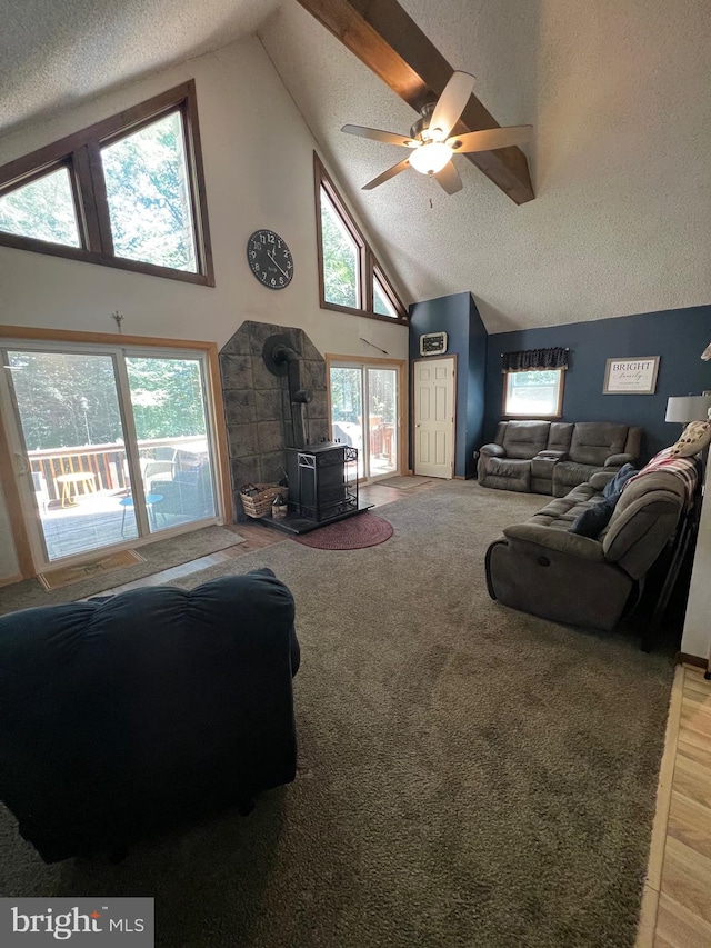 living room with a textured ceiling, ceiling fan, high vaulted ceiling, light hardwood / wood-style floors, and a wood stove