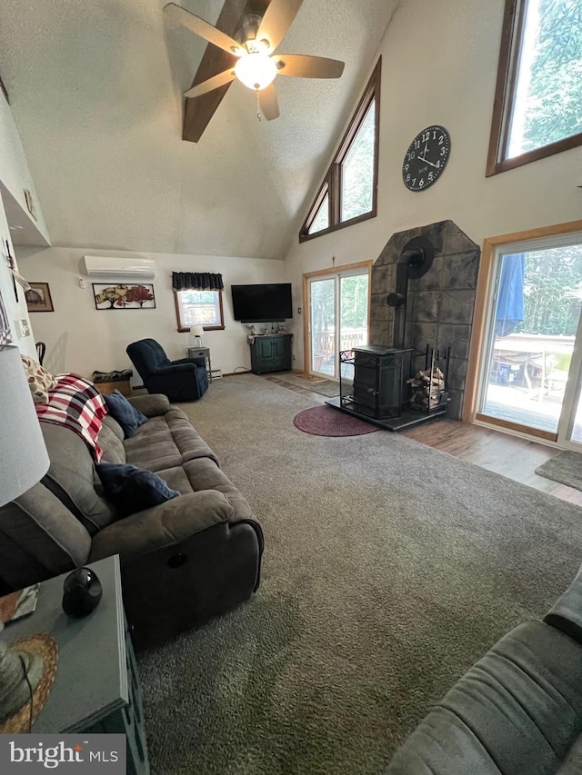 carpeted living room featuring a textured ceiling, ceiling fan, high vaulted ceiling, a wood stove, and a wall mounted AC