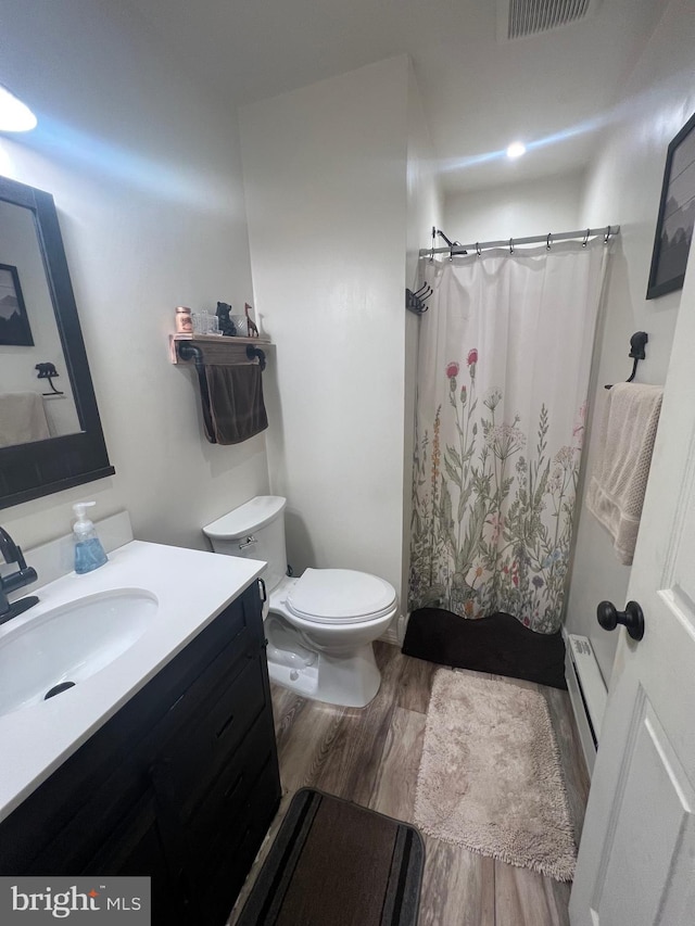 bathroom with hardwood / wood-style floors, a baseboard heating unit, vanity, and toilet