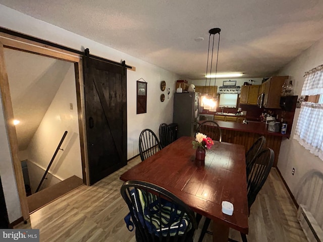 dining room with a barn door, a baseboard heating unit, light hardwood / wood-style flooring, and sink