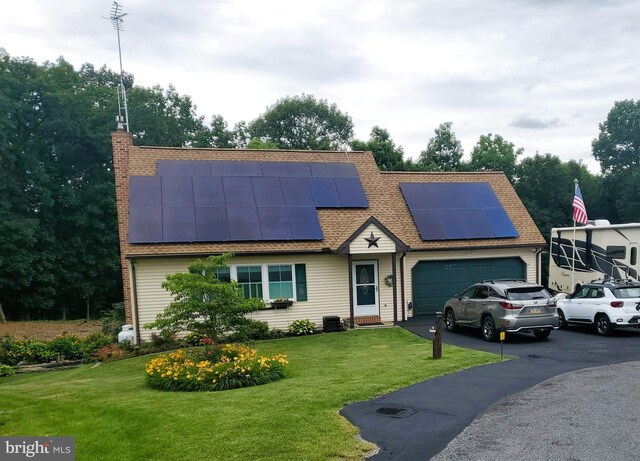 view of front of home with central AC, solar panels, a front yard, and a garage