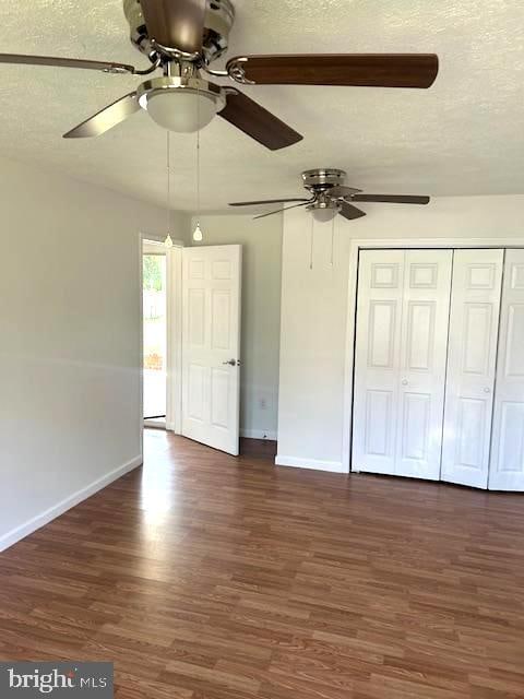 unfurnished bedroom featuring a closet, ceiling fan, dark hardwood / wood-style floors, and a textured ceiling