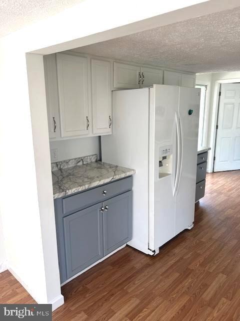 kitchen with light stone countertops, dark hardwood / wood-style flooring, gray cabinets, a textured ceiling, and white fridge with ice dispenser