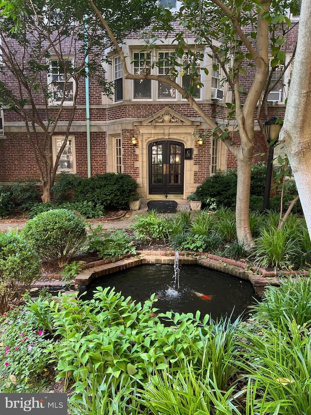 doorway to property with brick siding, a small pond, and french doors