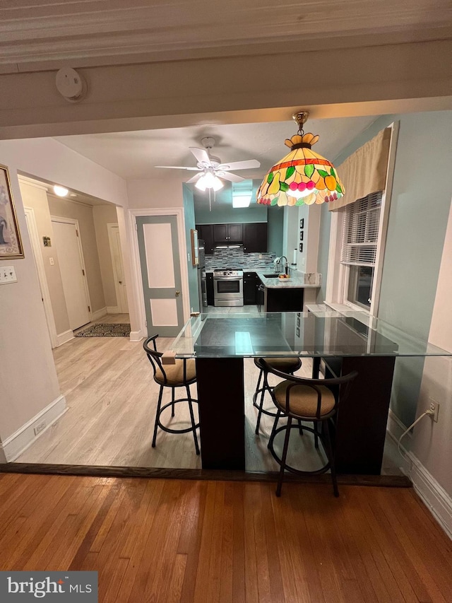 kitchen featuring decorative backsplash, stainless steel range, light wood-type flooring, and a sink