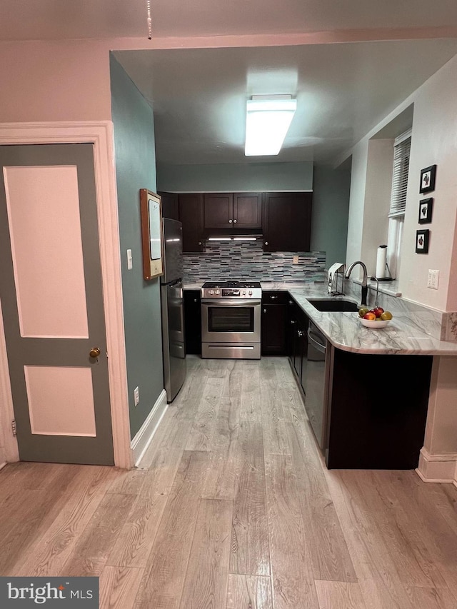 kitchen featuring a sink, under cabinet range hood, stainless steel appliances, light wood finished floors, and decorative backsplash