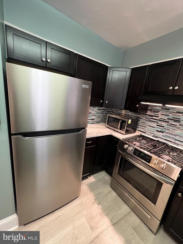 kitchen with tasteful backsplash, dark cabinets, and appliances with stainless steel finishes