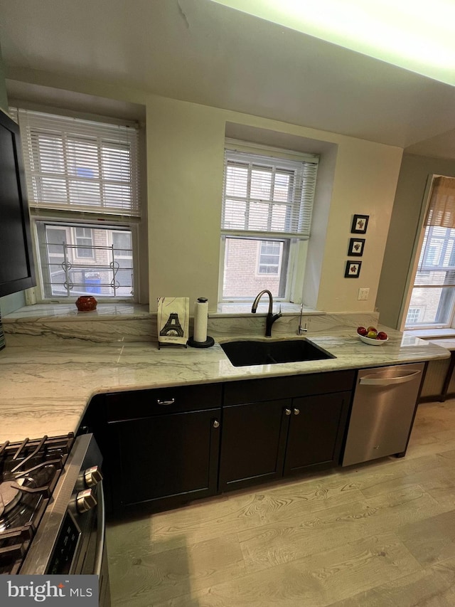 kitchen featuring light stone counters, stainless steel appliances, a sink, light wood-style floors, and dark cabinets