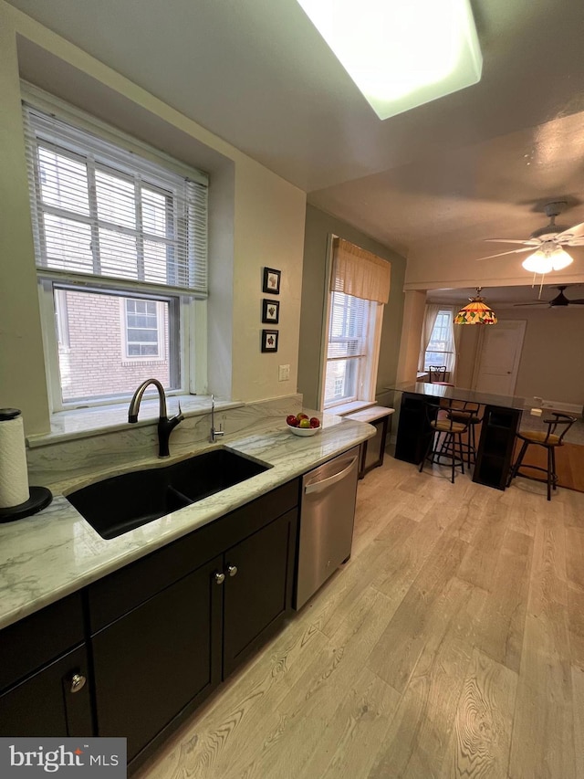 kitchen featuring light wood-style flooring, a sink, stainless steel dishwasher, light stone countertops, and dark cabinets