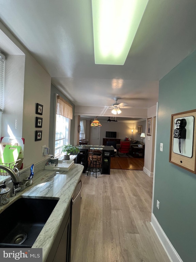 kitchen featuring light wood-type flooring, ceiling fan, sink, light stone countertops, and stainless steel dishwasher