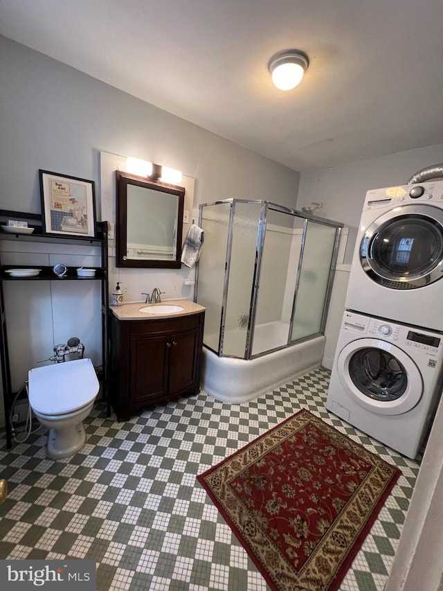 full bath featuring a shower with door, toilet, tile patterned floors, vanity, and stacked washer / drying machine