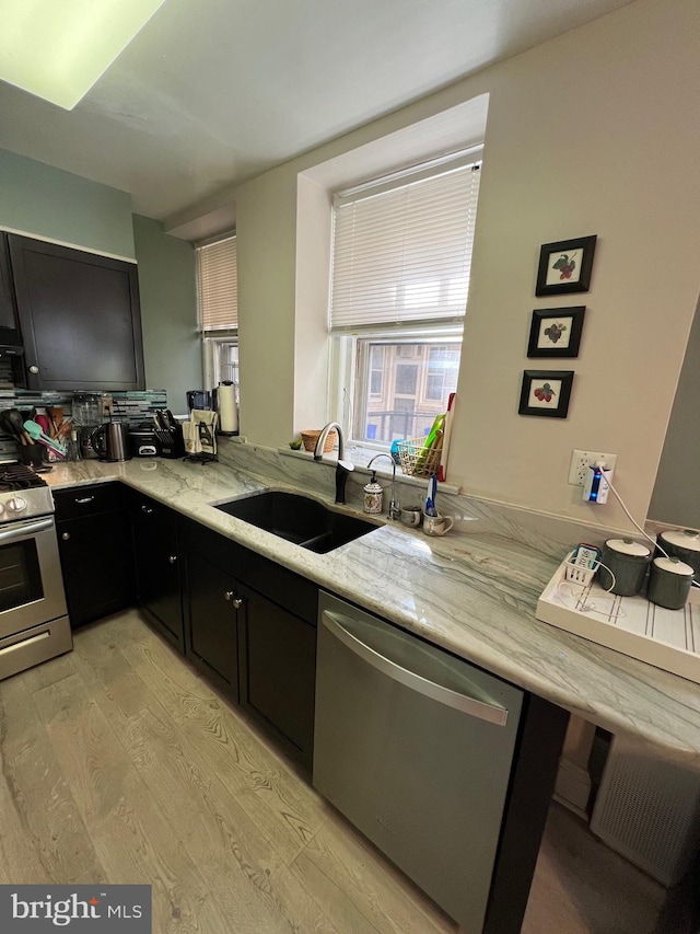 kitchen with light hardwood / wood-style flooring, sink, light stone counters, stainless steel appliances, and kitchen peninsula