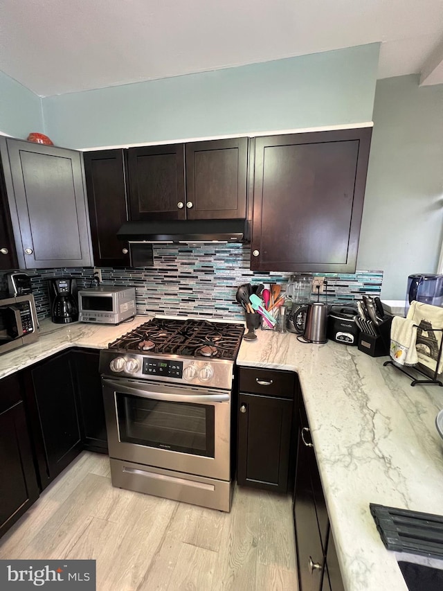 kitchen featuring light stone countertops, light wood-type flooring, decorative backsplash, and stainless steel range with gas stovetop