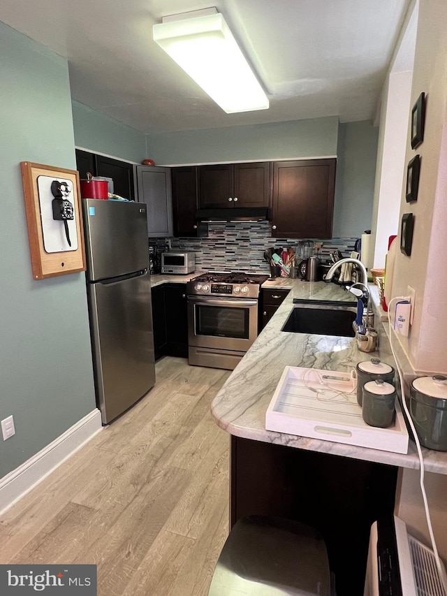 kitchen featuring light hardwood / wood-style flooring, sink, light stone counters, stainless steel appliances, and backsplash