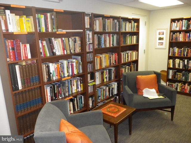 living area featuring wall of books and carpet floors